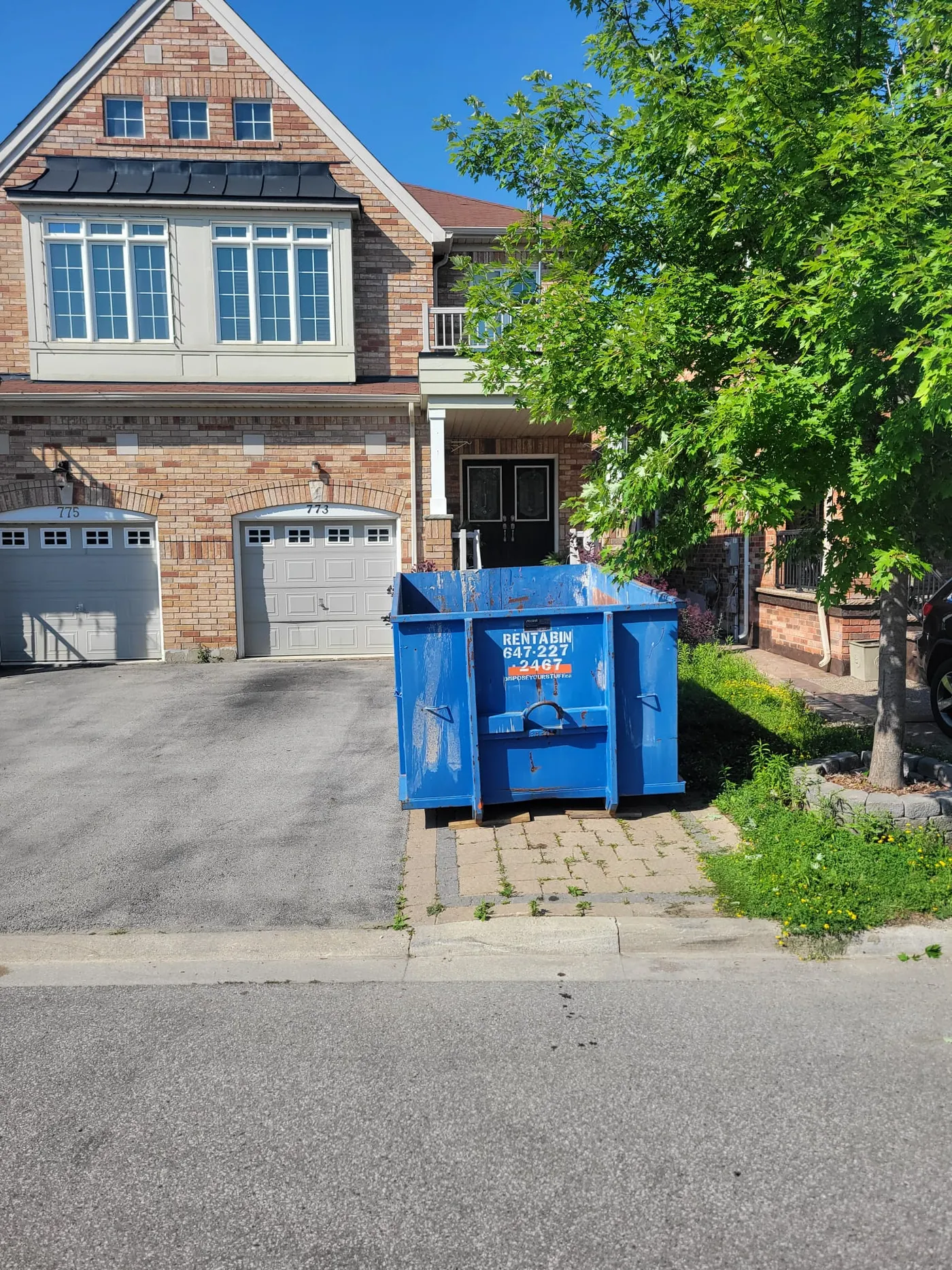 A large blue disposal bin on a driveway filled with yard waste, illustrating sorting requirements.