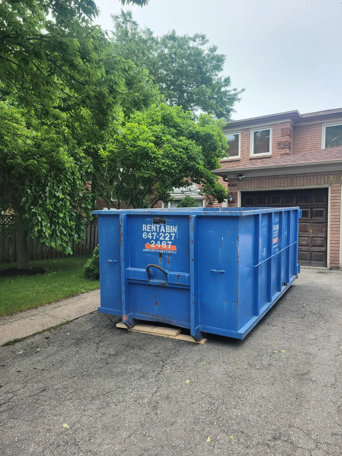 A clean blue disposal bin on a driveway with wooden protection boards